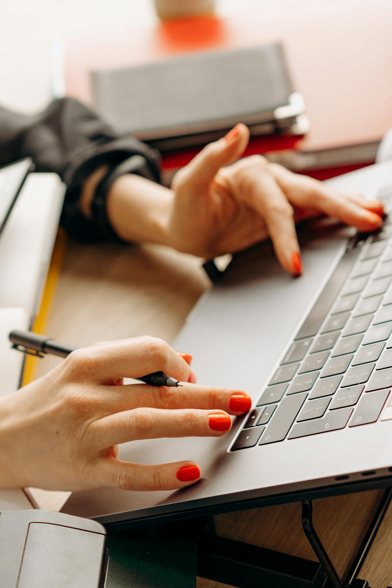 Close-up of hands with red nails typing on a laptop keyboard, depicting a productive work environment.